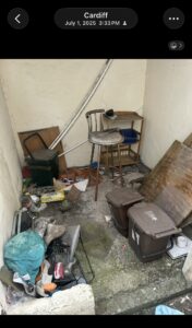 A dirty, cluttered storage nook with a metal chair, wooden shelf, and scattered trash and debris on the floor.